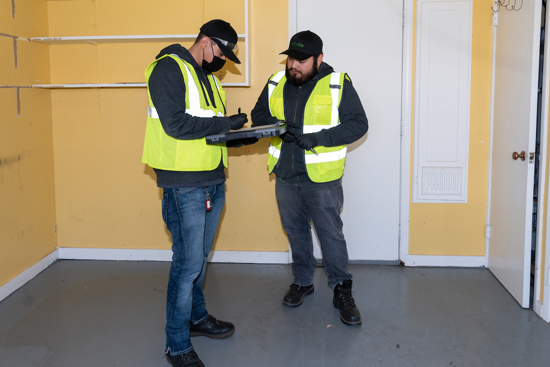Two Adviro environmental testing technicians discuss the tasks to be done for an asbestos survey project inside a vacant home in the San Francisco Bay Area.